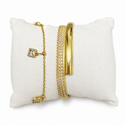 A premium two-piece gold-plated bracelet stack for women featuring a thick half-pavé crossover bangle and a fine chain bracelet with three dangling square crystal charms.