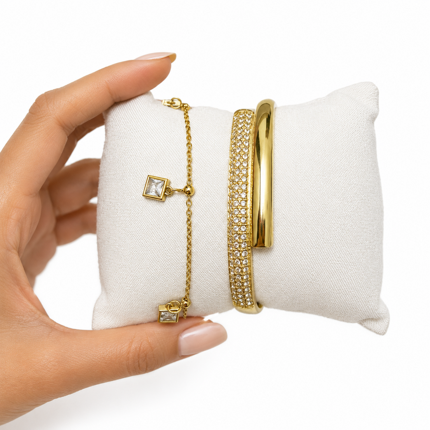 A close-view of a premium two-piece gold-plated bracelet stack for women featuring a thick half-pavé crossover bangle and a fine chain bracelet with three dangling square crystal charms.