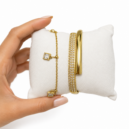 A close-view of a premium two-piece gold-plated bracelet stack for women featuring a thick half-pavé crossover bangle and a fine chain bracelet with three dangling square crystal charms.