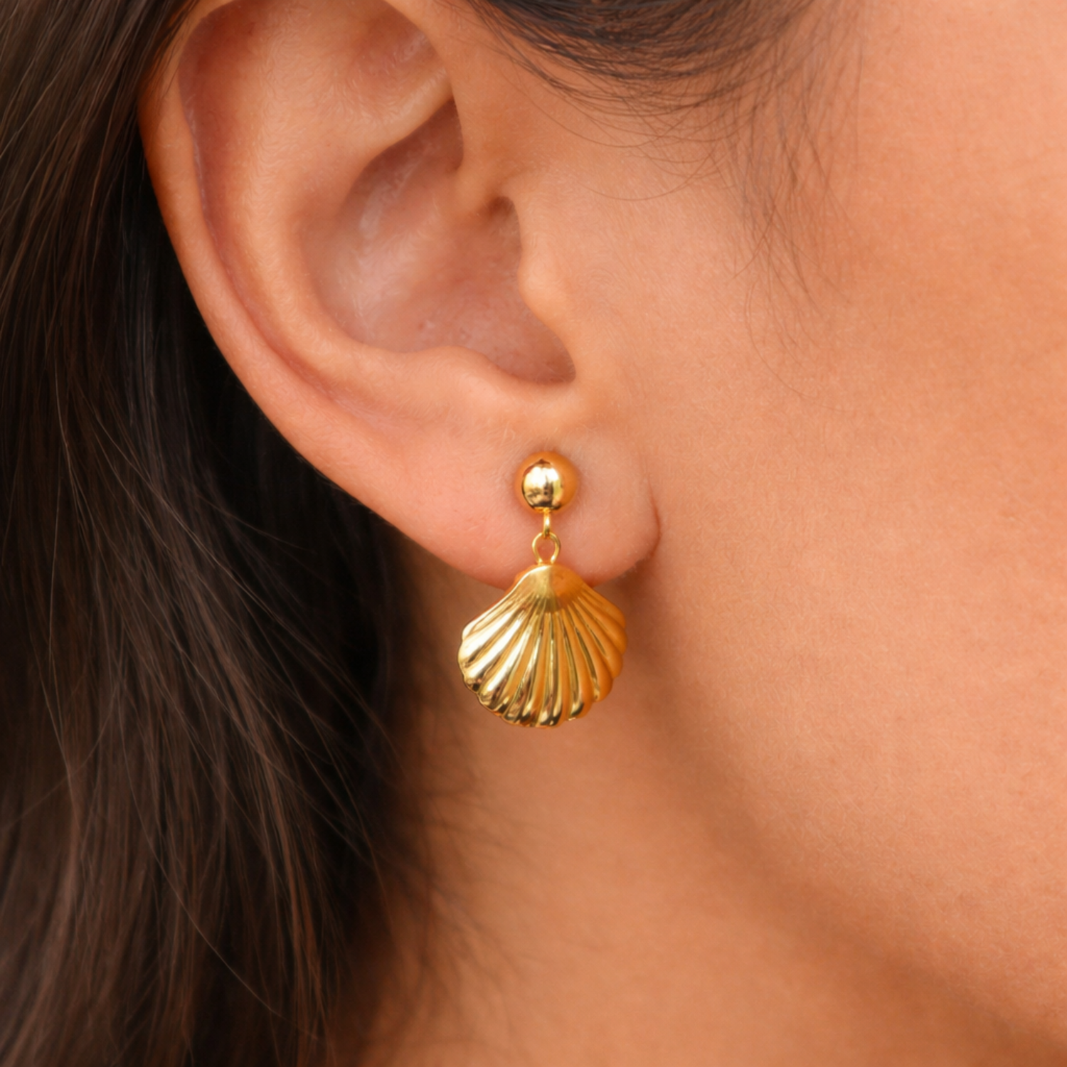 A gold-plated shell drop earrings for women, featuring a smooth gold stud and a textured shell pendant, shown on a model