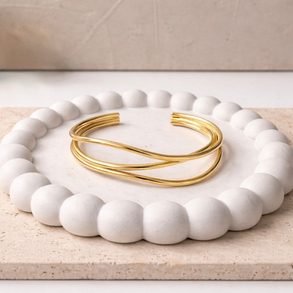 A bold and modern gold-plated triple-band adjustable cuff bracelet for women featuring an organic wave design, displayed on a white ceramic tray