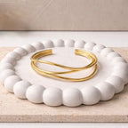 A bold and modern gold-plated triple-band adjustable cuff bracelet for women featuring an organic wave design, displayed on a white ceramic tray