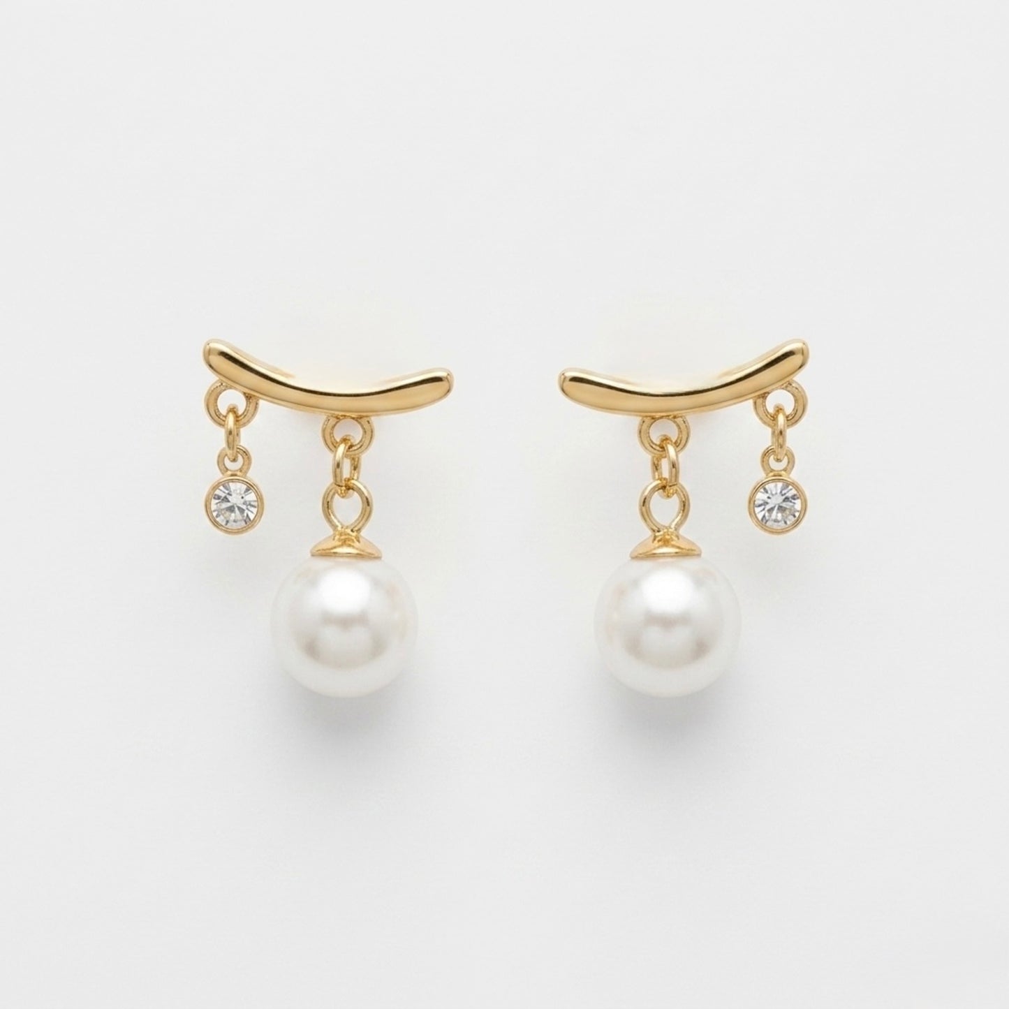 A pair of gold-plated arc drop earrings for women featuring a central white pearl and a small clear crystal, shown on a white background.