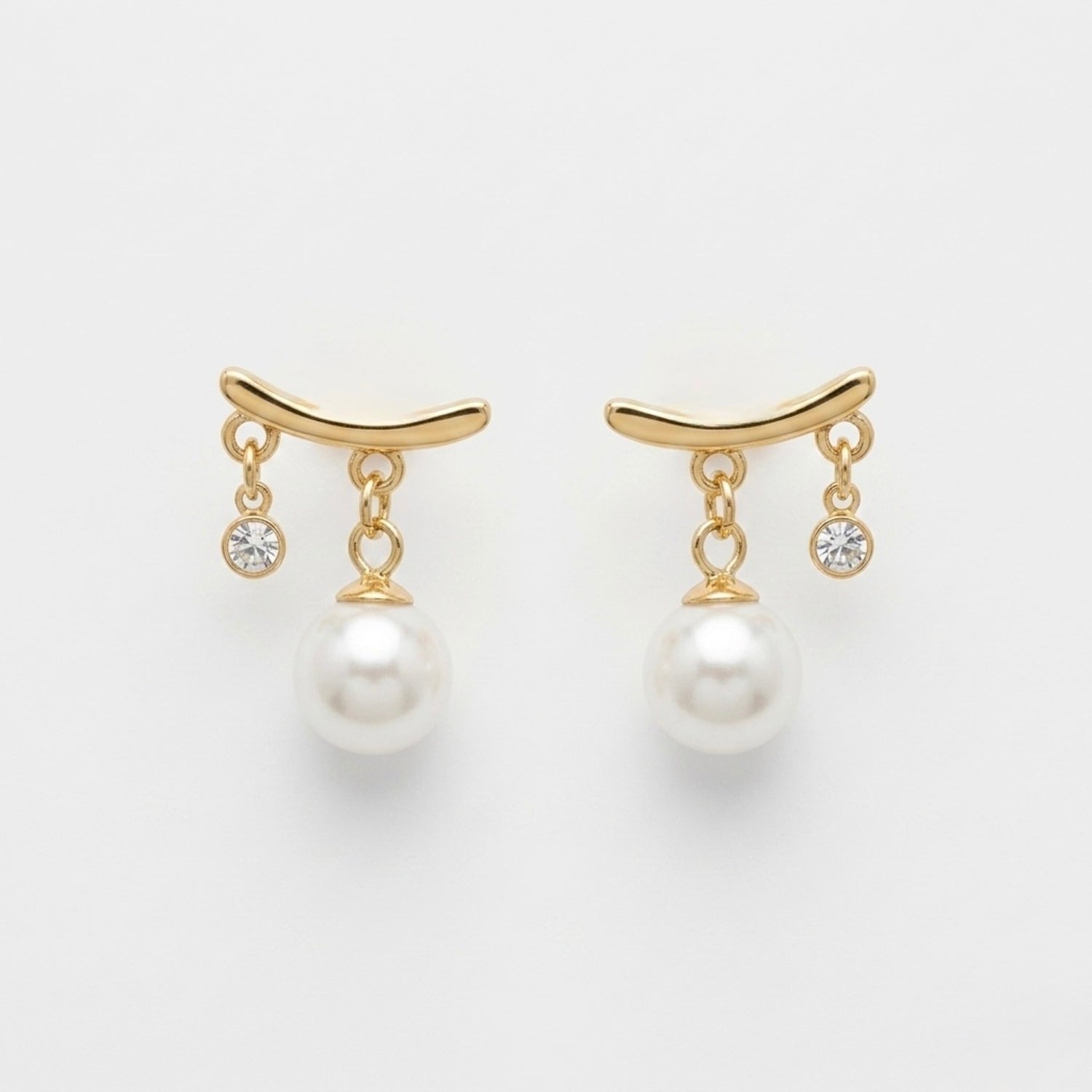A pair of gold-plated arc drop earrings for women featuring a central white pearl and a small clear crystal, shown on a white background.