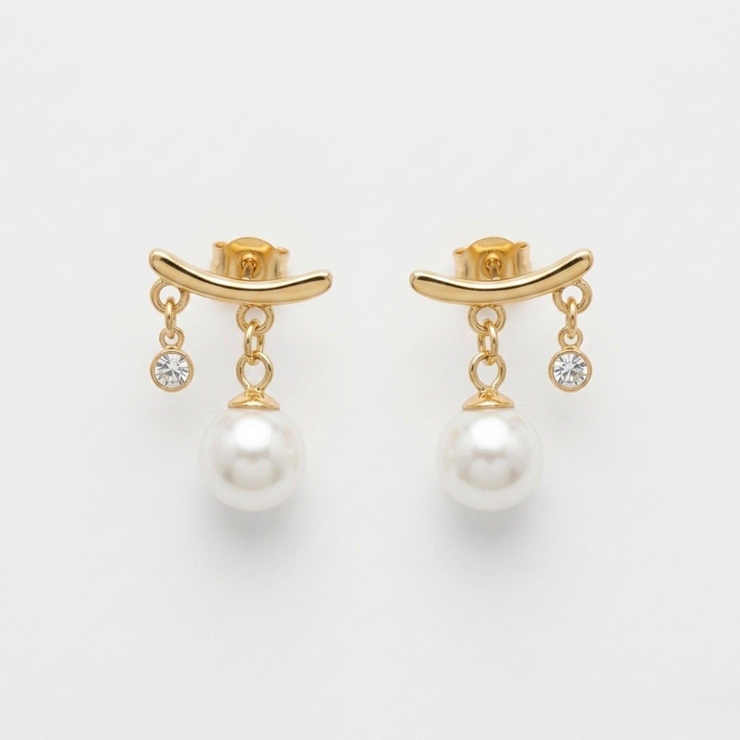 A close-view of a pair of gold-plated arc drop earrings for women featuring a central white pearl and a small clear crystal, shown on a white background
