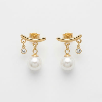 A close-view of a pair of gold-plated arc drop earrings for women featuring a central white pearl and a small clear crystal, shown on a white background