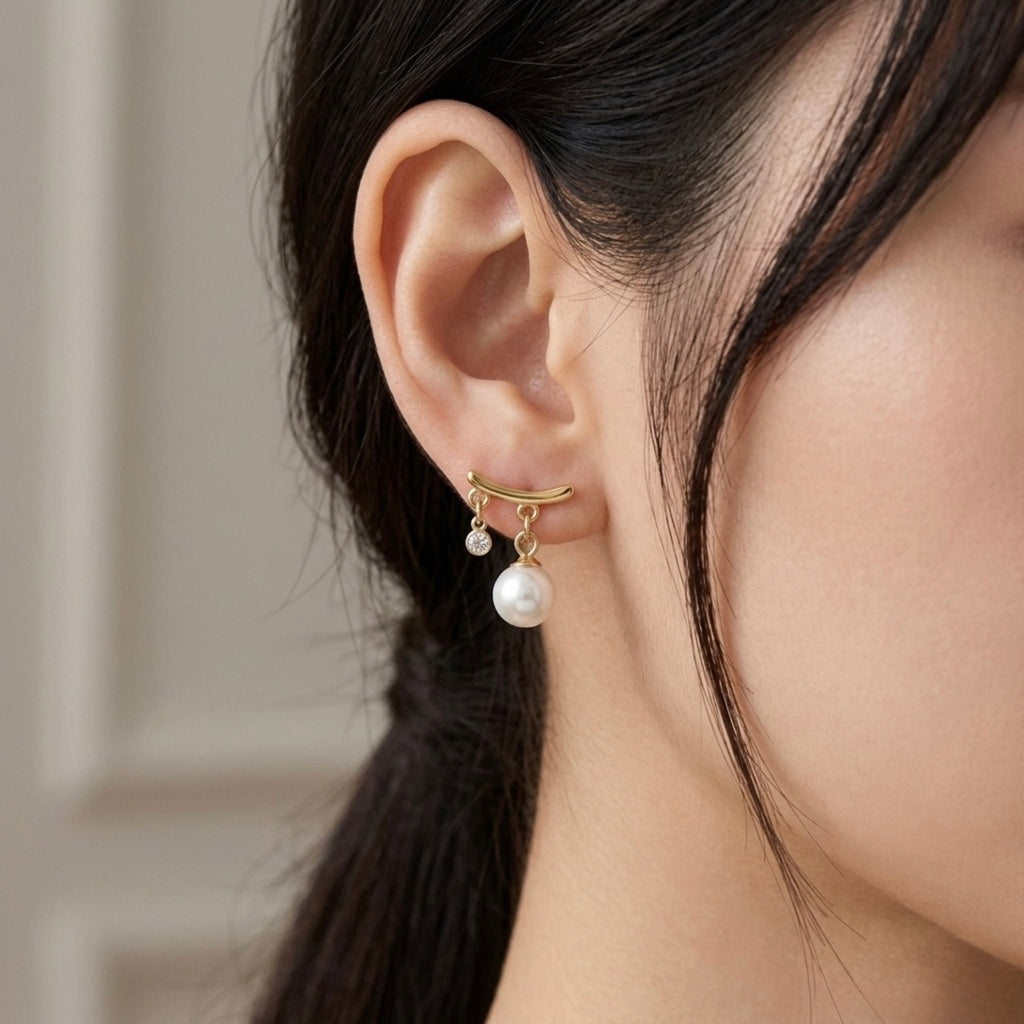 A gold-plated arc drop earrings for women featuring a central white pearl and a small clear crystal, shown on a model