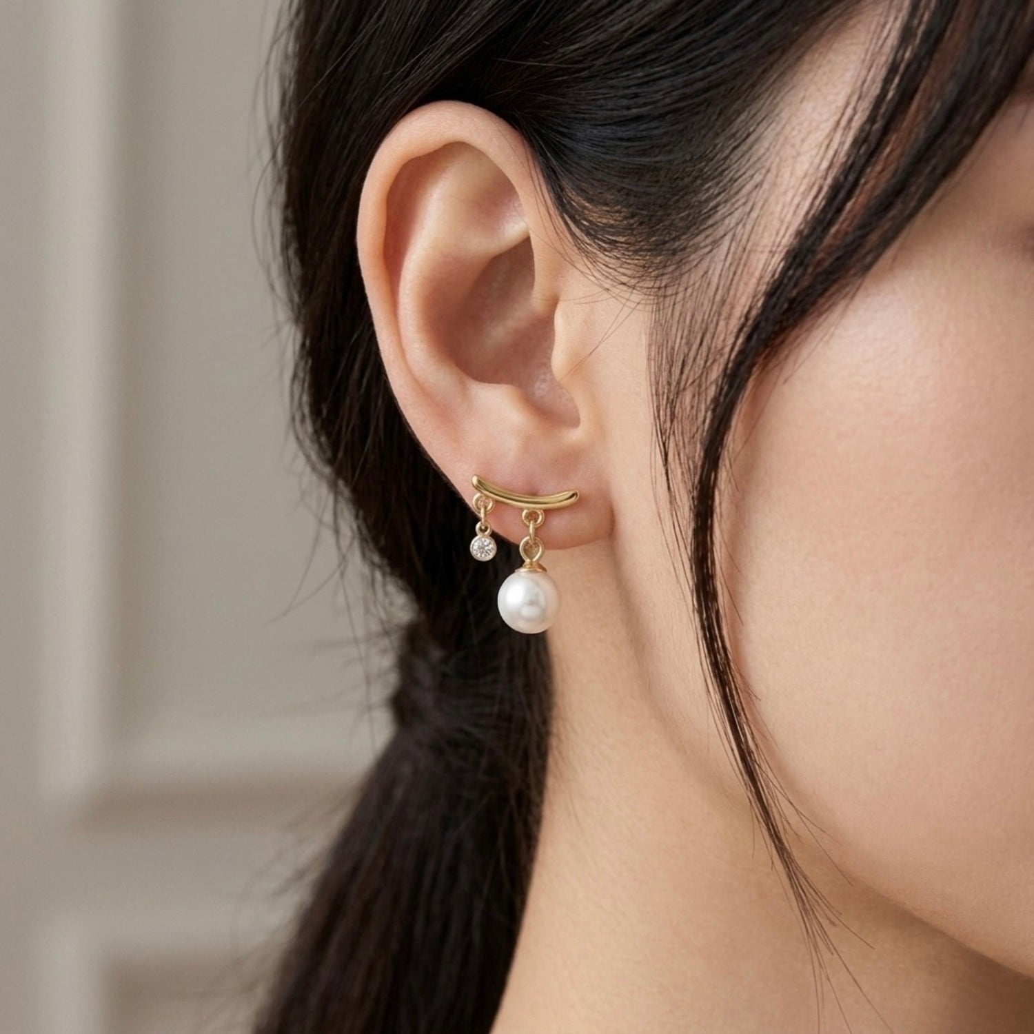 A gold-plated arc drop earrings for women featuring a central white pearl and a small clear crystal, shown on a model