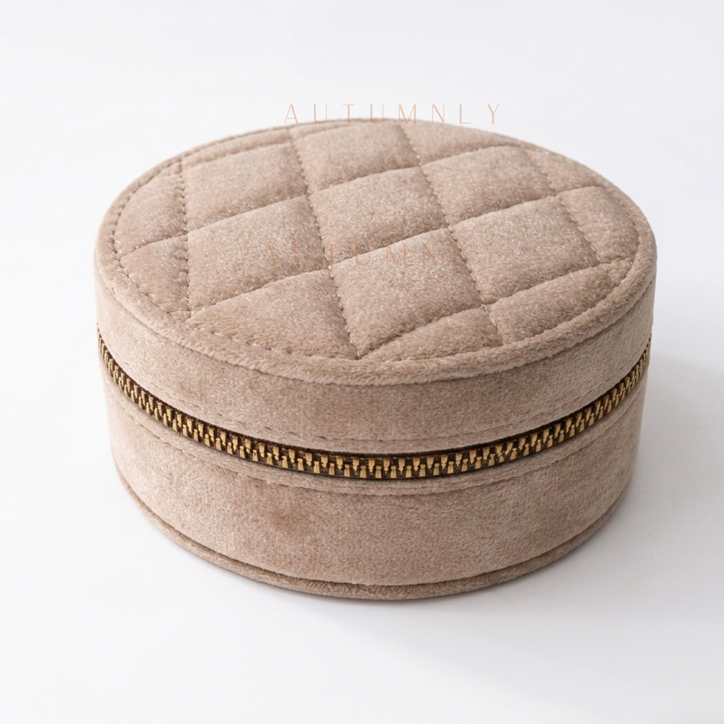 Round quilted beige jewelry box with a gold zipper on a white background