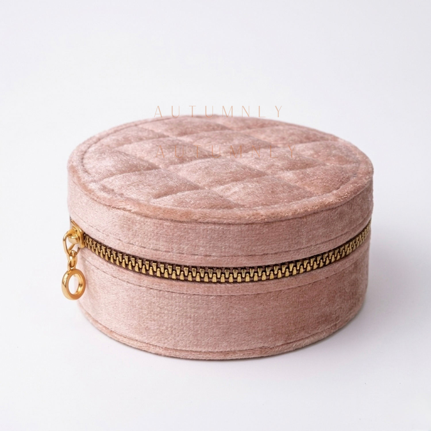 Blush pink round quilted jewelry box with a gold zipper on a white background