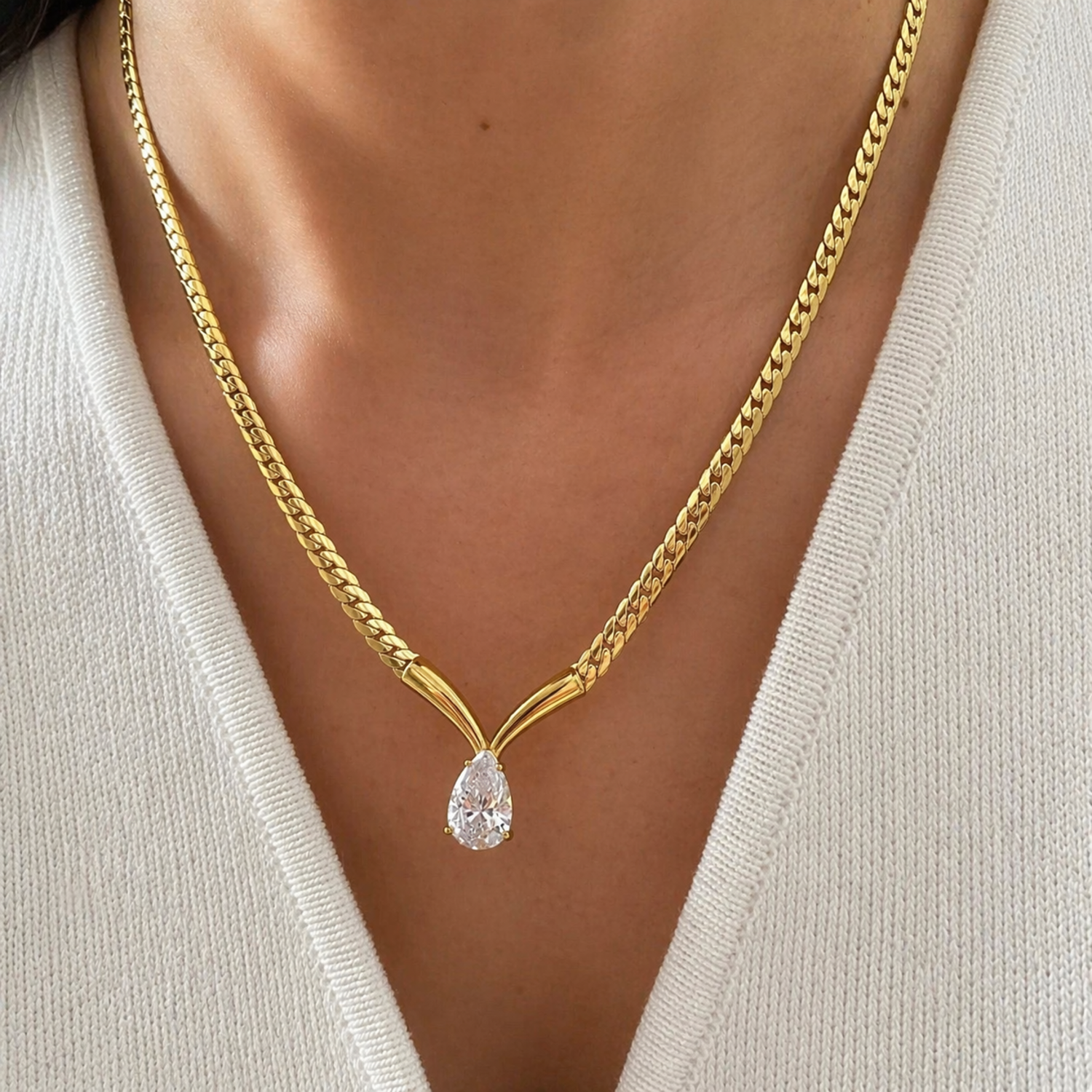 A gold-plated stainless steel chain for women featuring a V-shaped mounting and a large sparkling teardrop crystal pendant, shown on a model