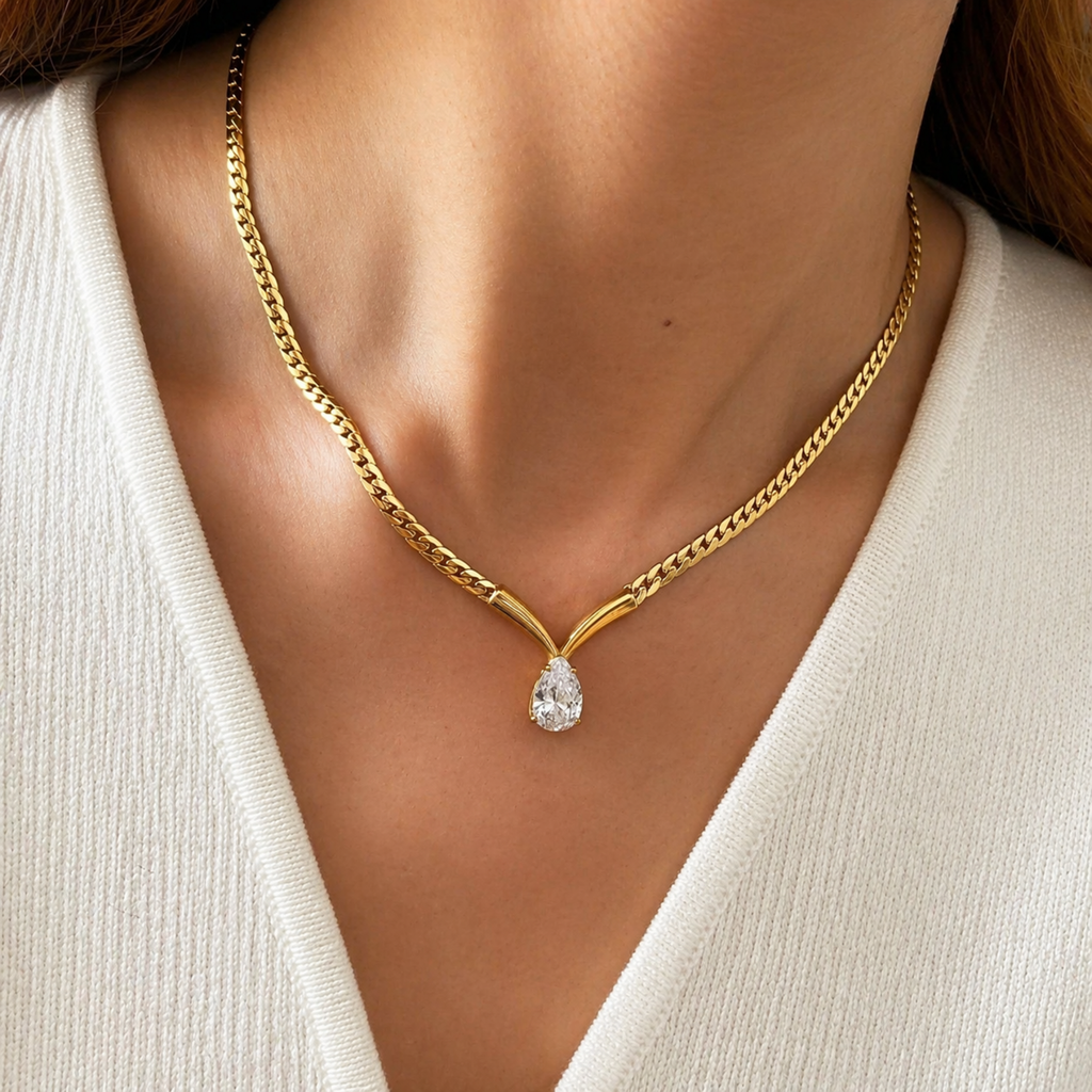 A gold-plated stainless steel chain for women featuring a V-shaped mounting and a large sparkling teardrop crystal pendant, shown on a model