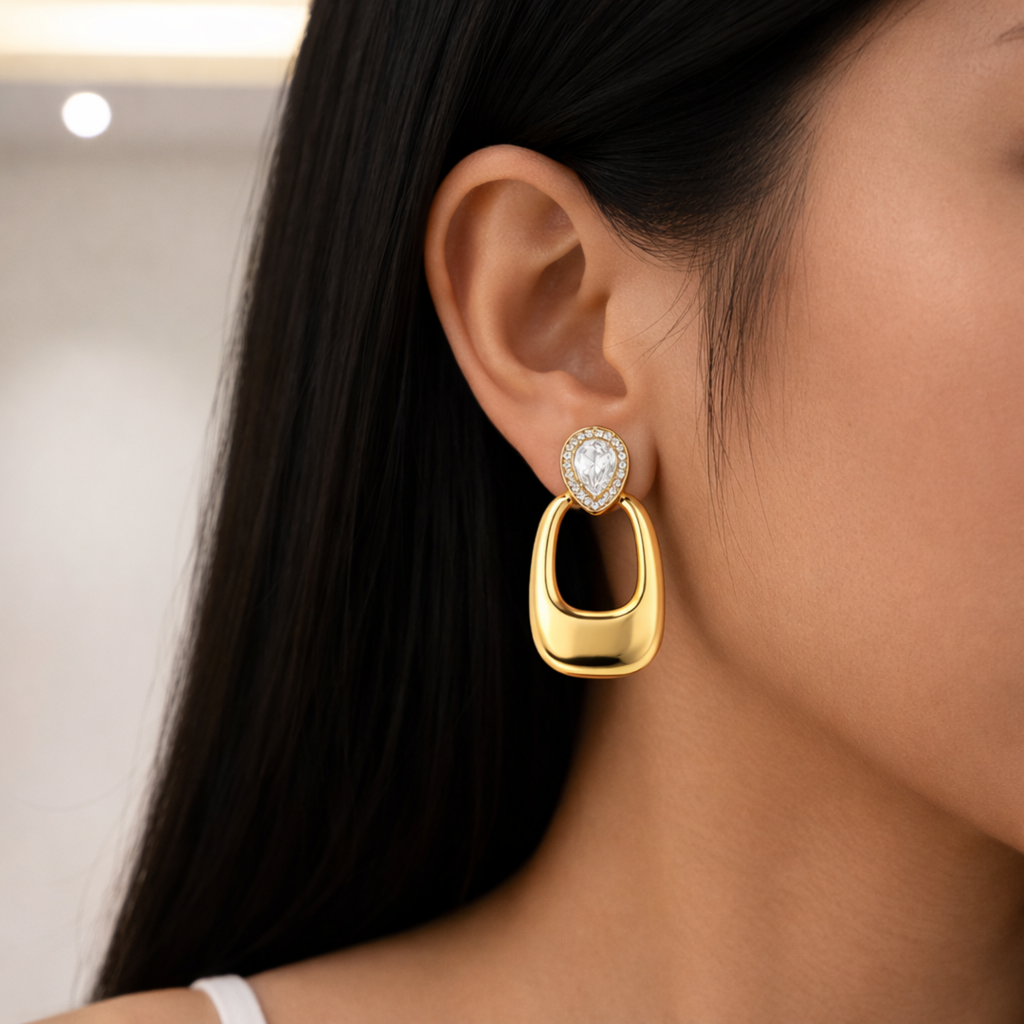 A gold-plated long earrings for women featuring a pear-cut crystal halo stud and a large, smooth rectangular golden drop shown on a model