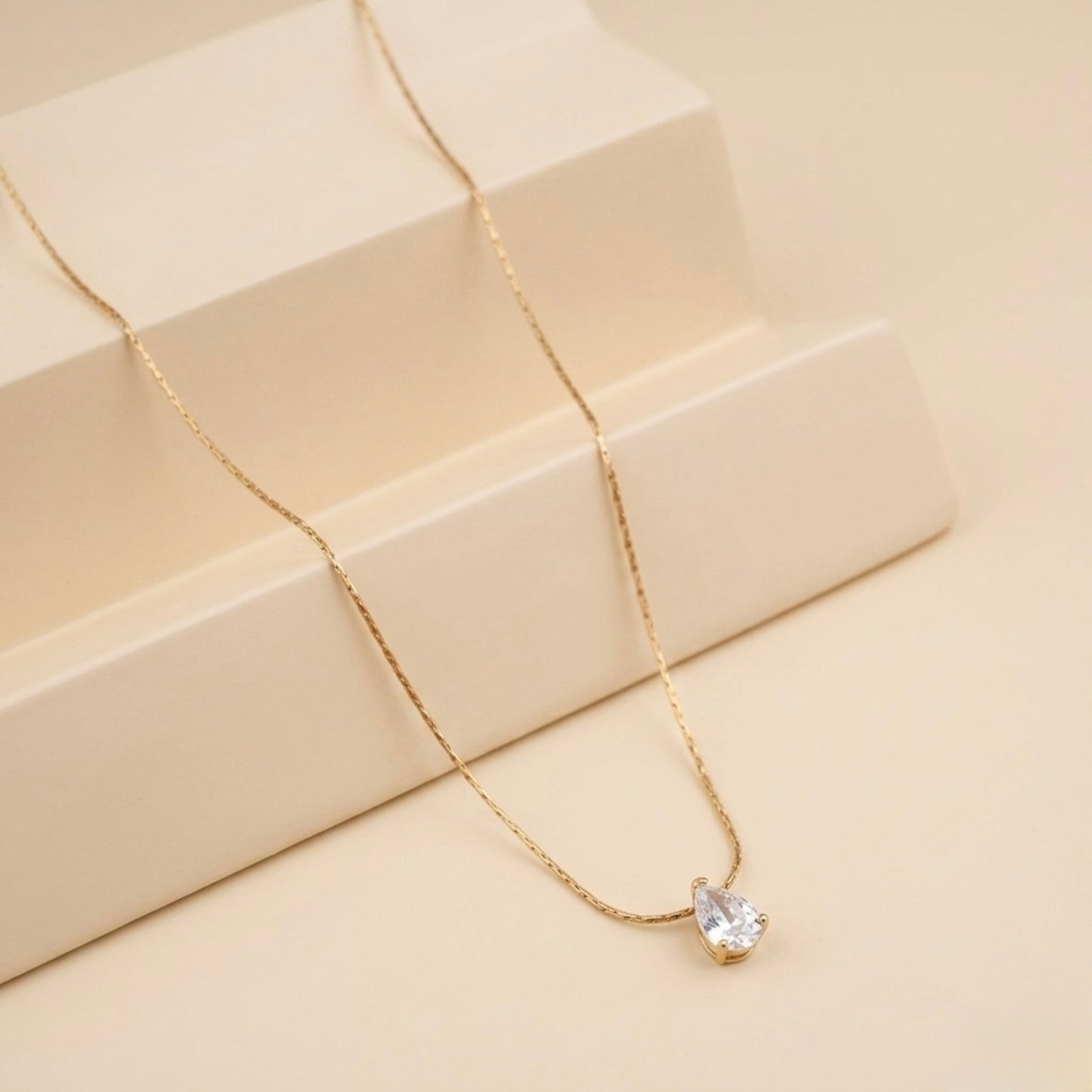 A close-view of a gold-plated stainless steel chain for women featuring a single, brilliant pear-cut crystal pendant on a delicate link chain.