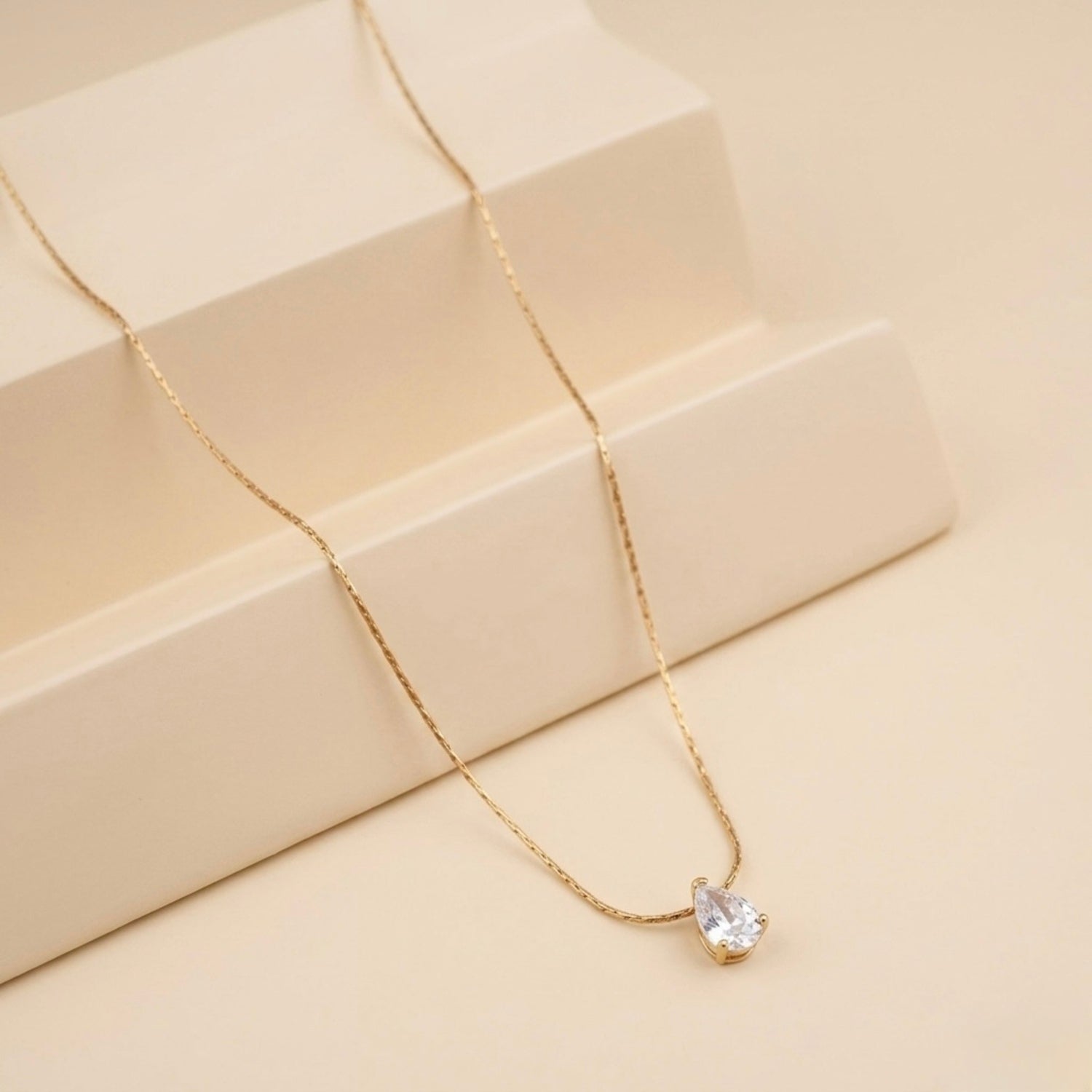A close-view of a gold-plated stainless steel chain for women featuring a single, brilliant pear-cut crystal pendant on a delicate link chain.