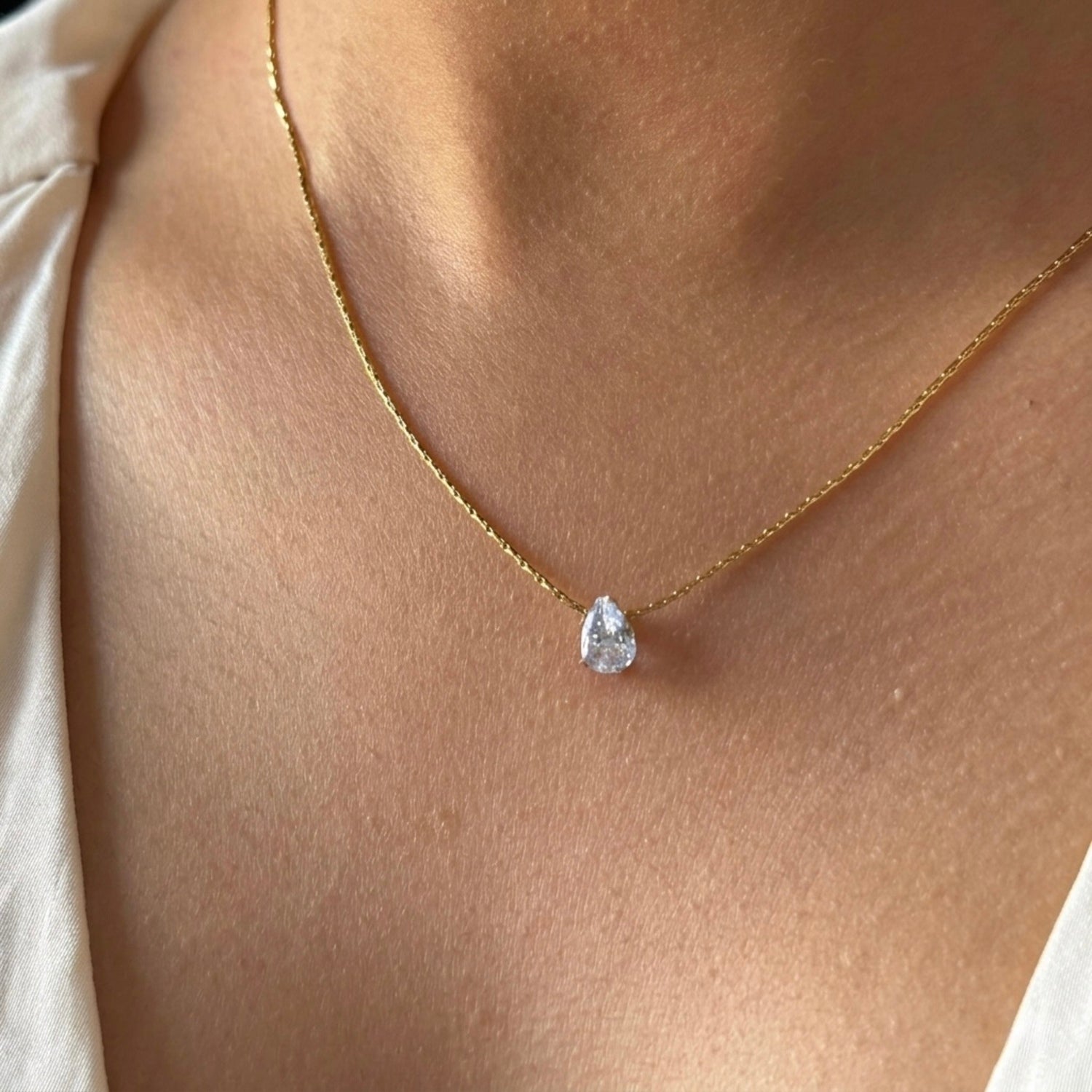 A gold-plated stainless steel chain for women featuring a single, brilliant pear-cut crystal pendant on a delicate link chain shown on a model