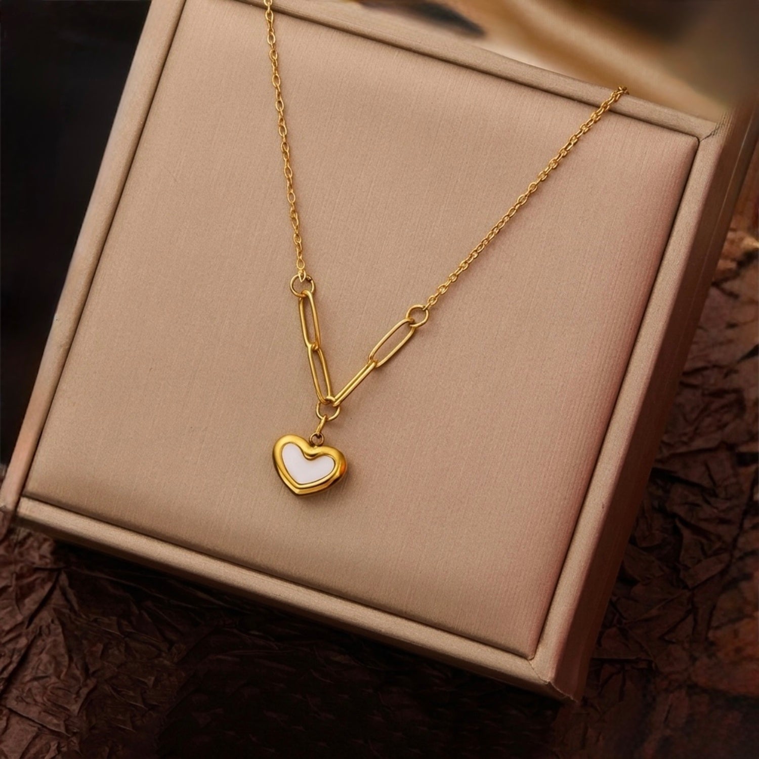 A gold-plated stainless steel chain for women featuring a heart-shaped pendant with a pearl inlay, suspended from elongated paperclip links and a delicate chain displayed on a showcase