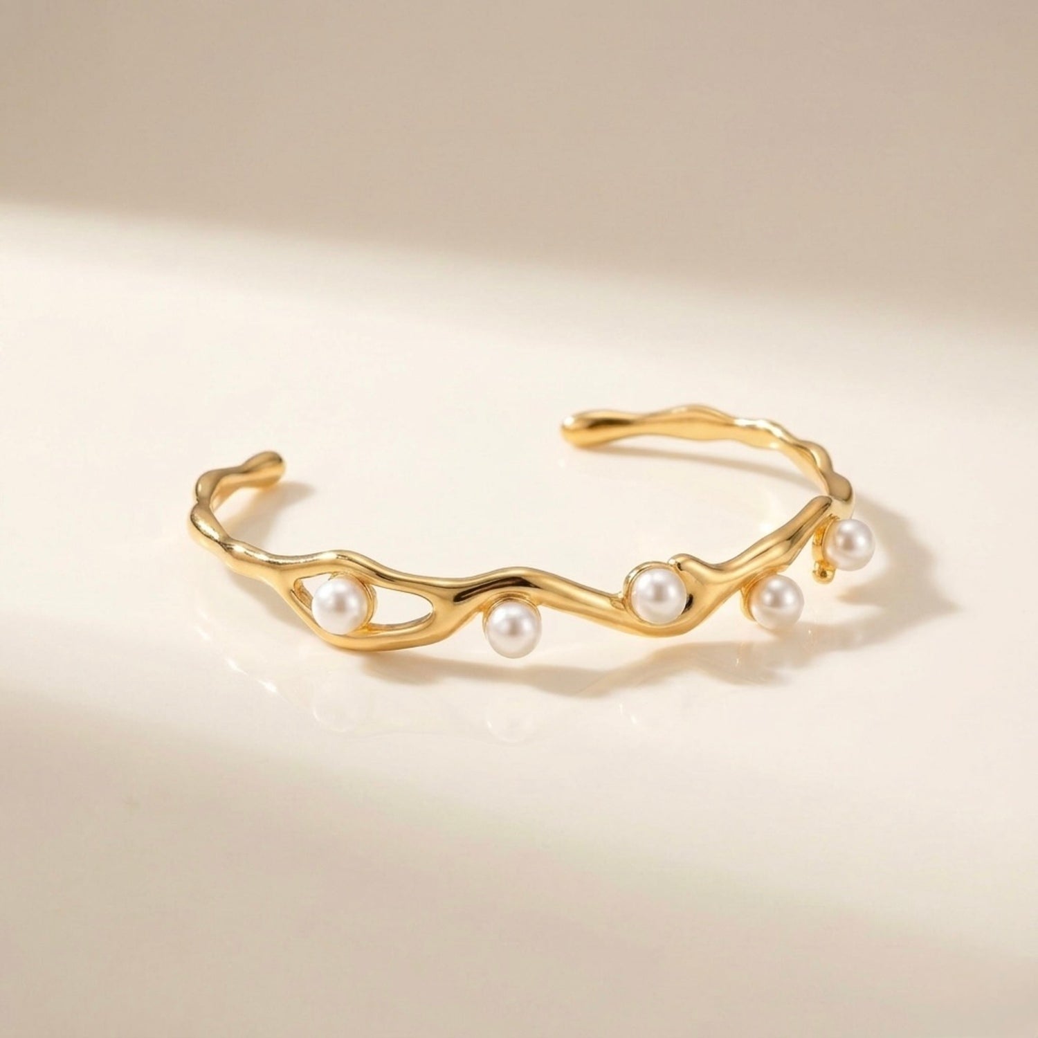 A gold-plated wave cuff bangle for women featuring five set pearls