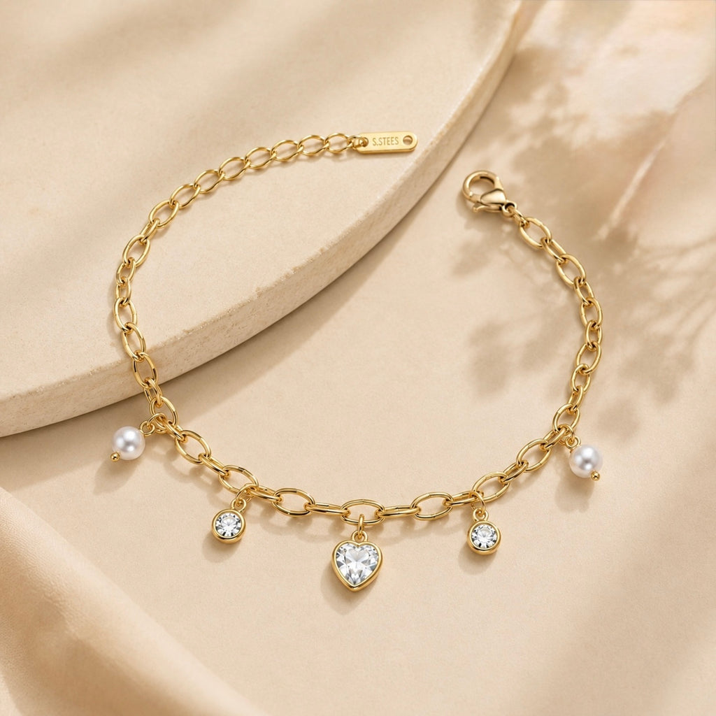 A gold-plated chain bracelet for women featuring dangling pearl charms, round crystals, and a central heart-shaped crystal pendant.