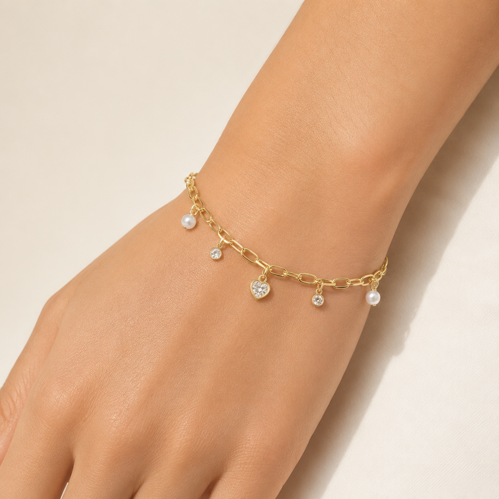 A gold-plated chain bracelet for women featuring dangling pearl charms, round crystals, and a central heart-shaped crystal pendant, shown on a model