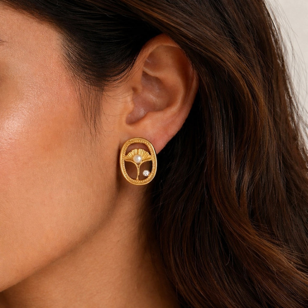 A gold-plated oval stud earrings for women featuring an shell design with a central pearl and a small crystal, shown on a model