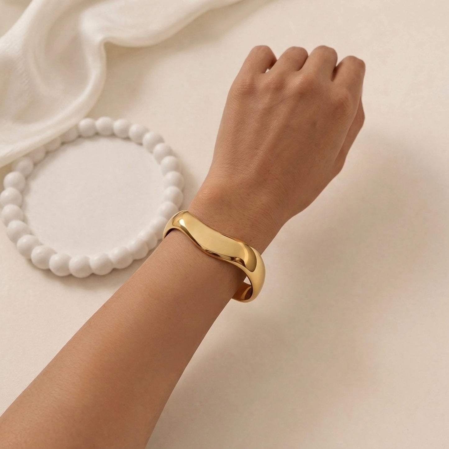 A bold and wide gold-plated organic wave cuff bracelet for women with a smooth, thick finish on a model hand