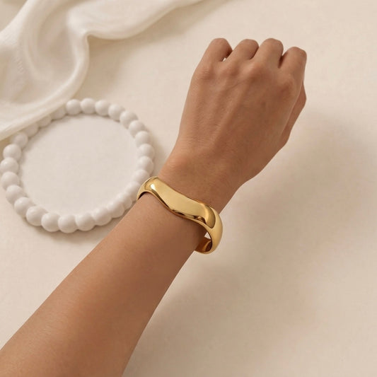 A bold and wide gold-plated organic wave cuff bracelet for women with a smooth, thick finish on a model hand