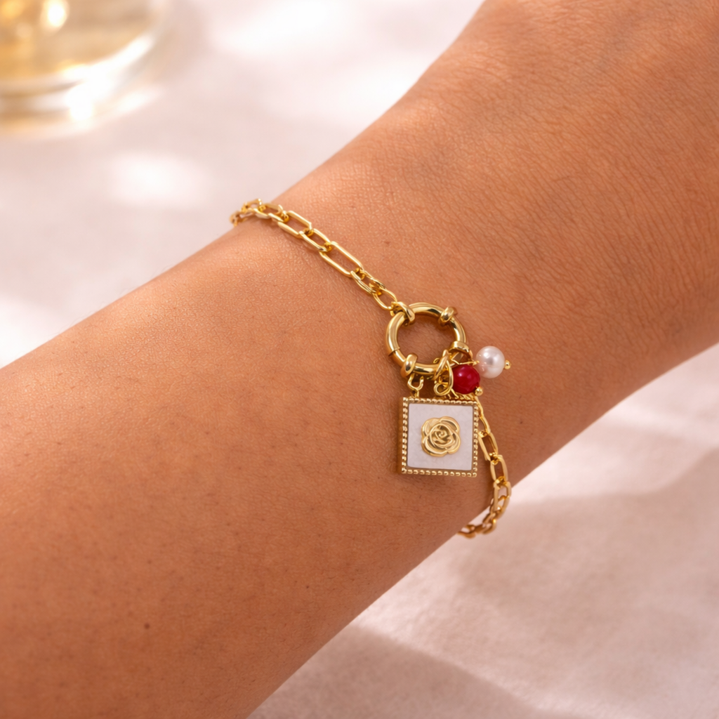 A gold-plated paperclip chain bracelet for women featuring a toggle clasp with rose, red bead, and pearl charms, shown on a model