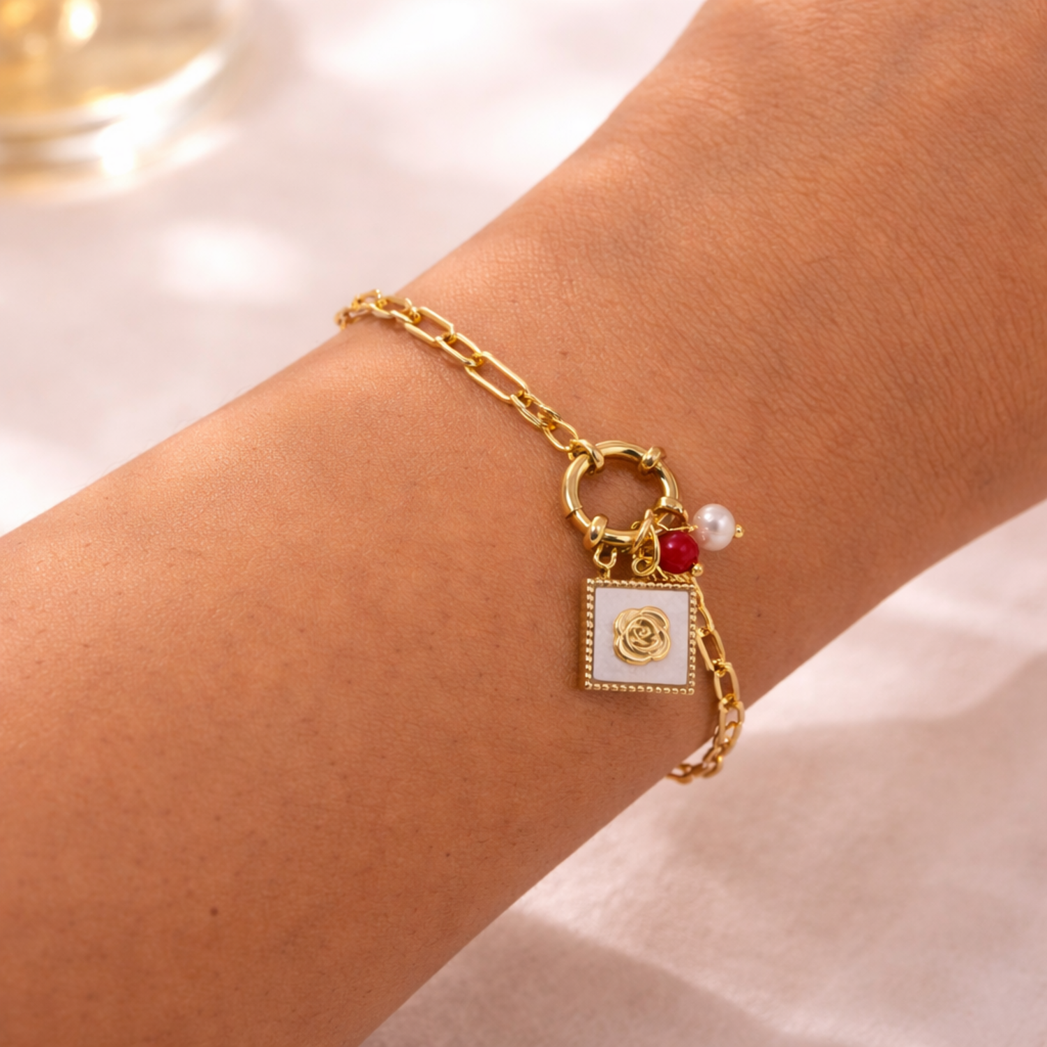 A gold-plated paperclip chain bracelet for women featuring a toggle clasp with rose, red bead, and pearl charms, shown on a model