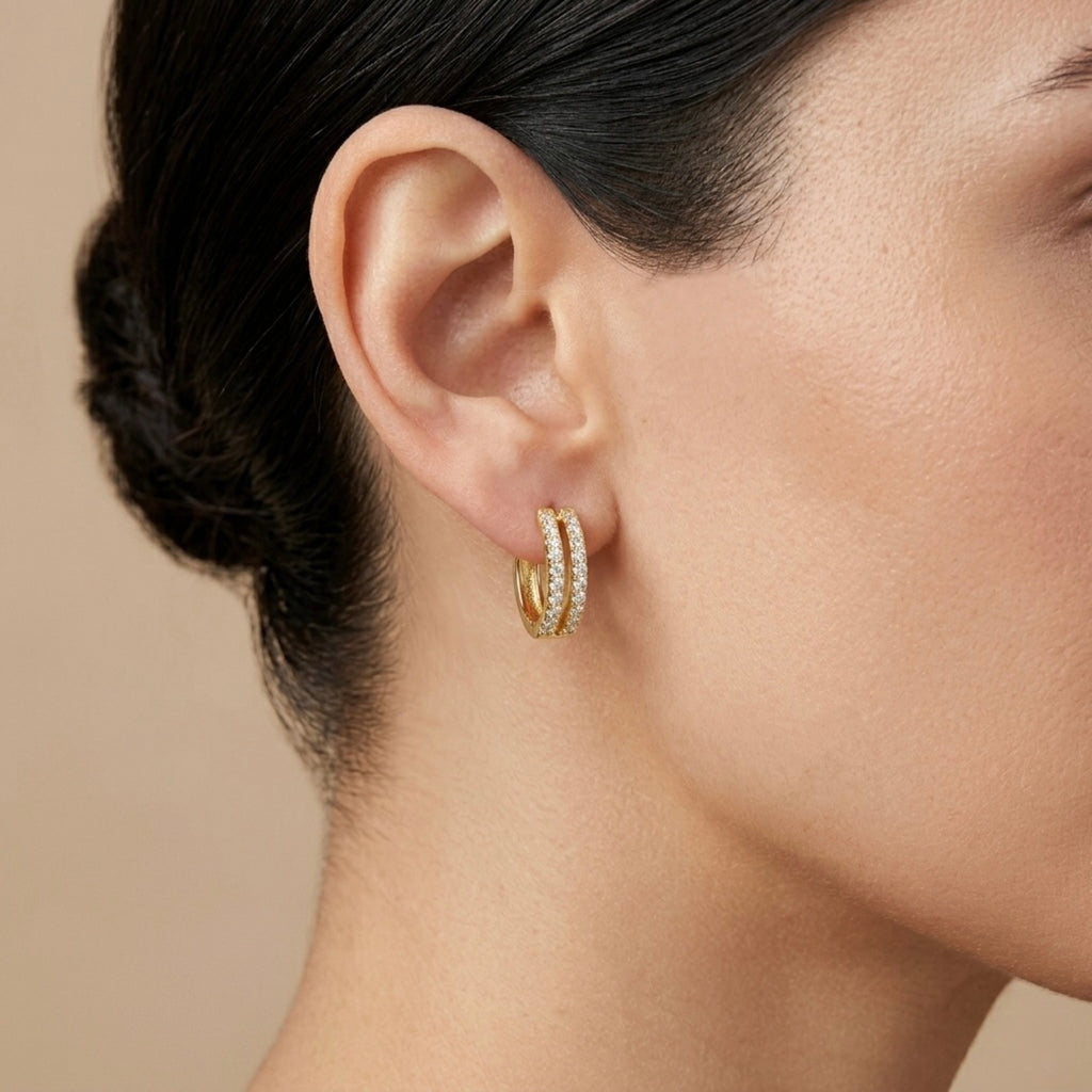 A gold-plated huggie hoop earrings for women featuring two parallel rows of clear crystals, shown on a model