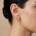 A gold-plated huggie hoop earrings for women featuring two parallel rows of clear crystals, shown on a model