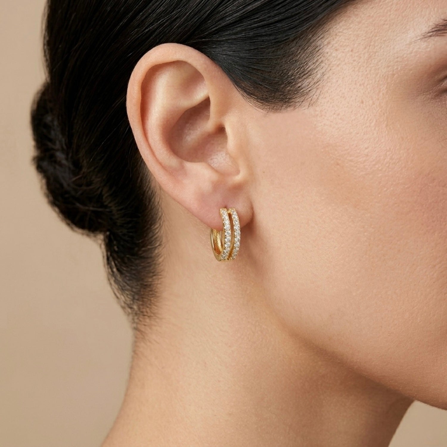 A gold-plated huggie hoop earrings for women featuring two parallel rows of clear crystals, shown on a model