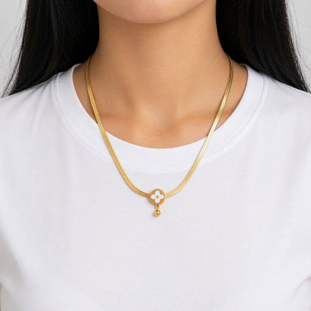A gold-plated stainless steel chain for women featuring a flat high-shine texture and an open clover pendant with a small gold drop shown on a model