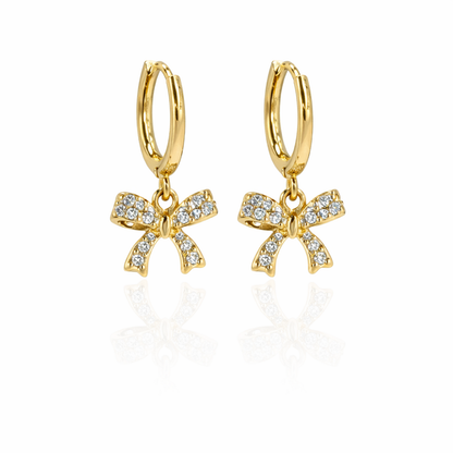 A pair of gold-plated hoop earrings for women featuring a sparkling crystal-encrusted bow drop, shown on a white background