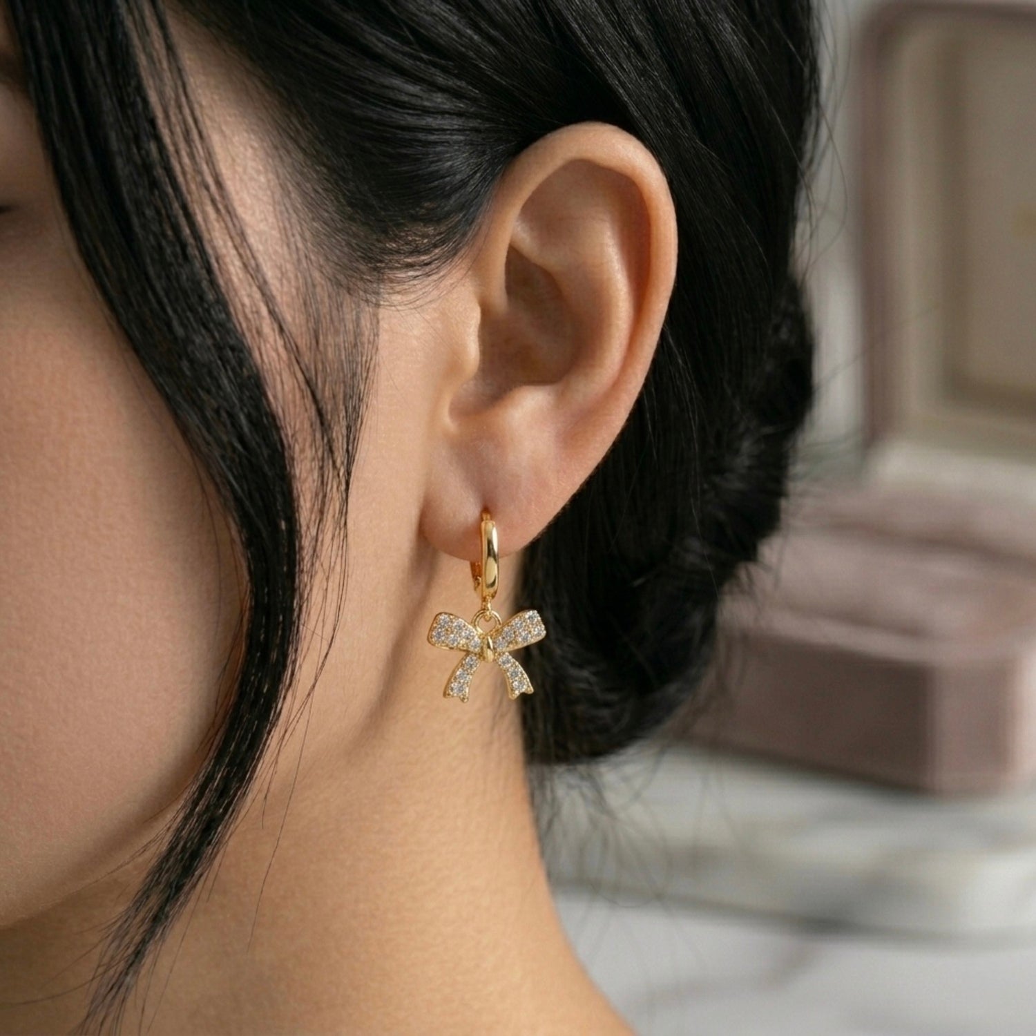 A gold-plated hoop earrings for women featuring a sparkling crystal-encrusted bow drop, shown on a model