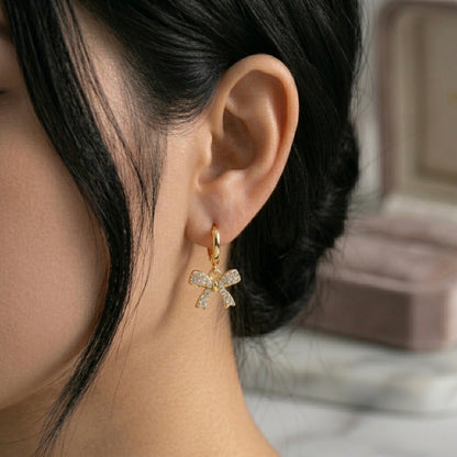 A gold-plated hoop earrings for women featuring a sparkling crystal-encrusted bow drop, shown on a model