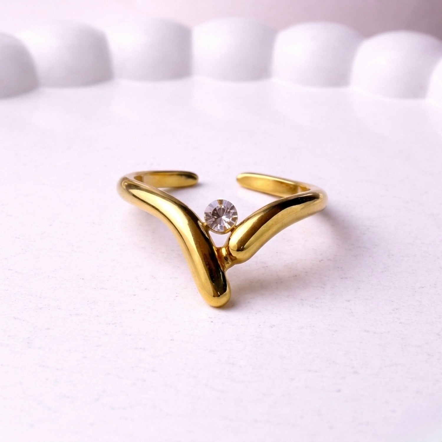 Gold plated ring with a white stone at the centre a white background