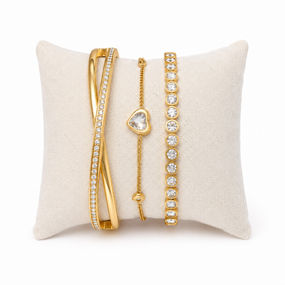 A premium three-piece gold-plated bracelet stack for women featuring a half-pavé crossover bangle, a sleek bezel-set crystal bangle, and a fine link chain with a single heart crystal charm