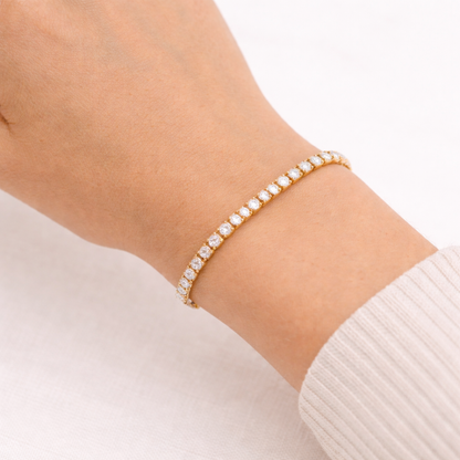 A classic gold-plated tennis bracelet for women on a wrist featuring a continuous row of brilliant round-cut stones, shown on a white background
