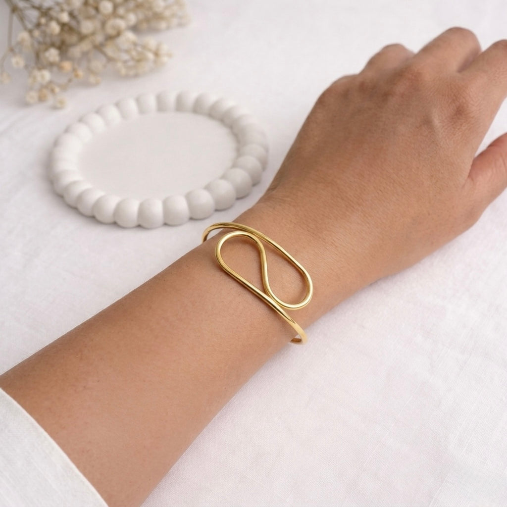 A close-view of a modern gold-plated adjustable cuff bracelet for women featuring a sculptural infinite loop design