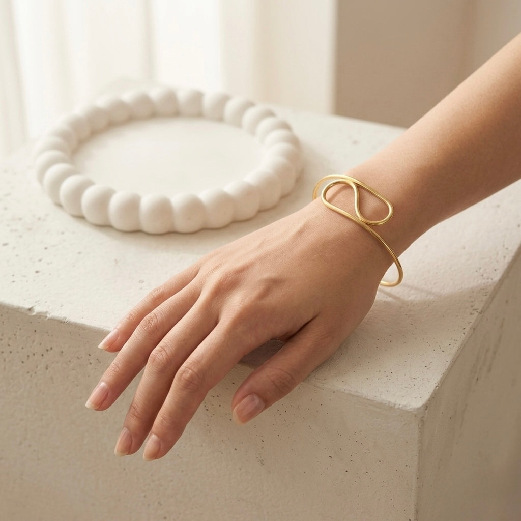 A modern gold-plated adjustable cuff bracelet for women featuring a sculptural infinite loop design, displayed on a model hand