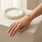 A modern gold-plated adjustable cuff bracelet for women featuring a sculptural infinite loop design, displayed on a model hand