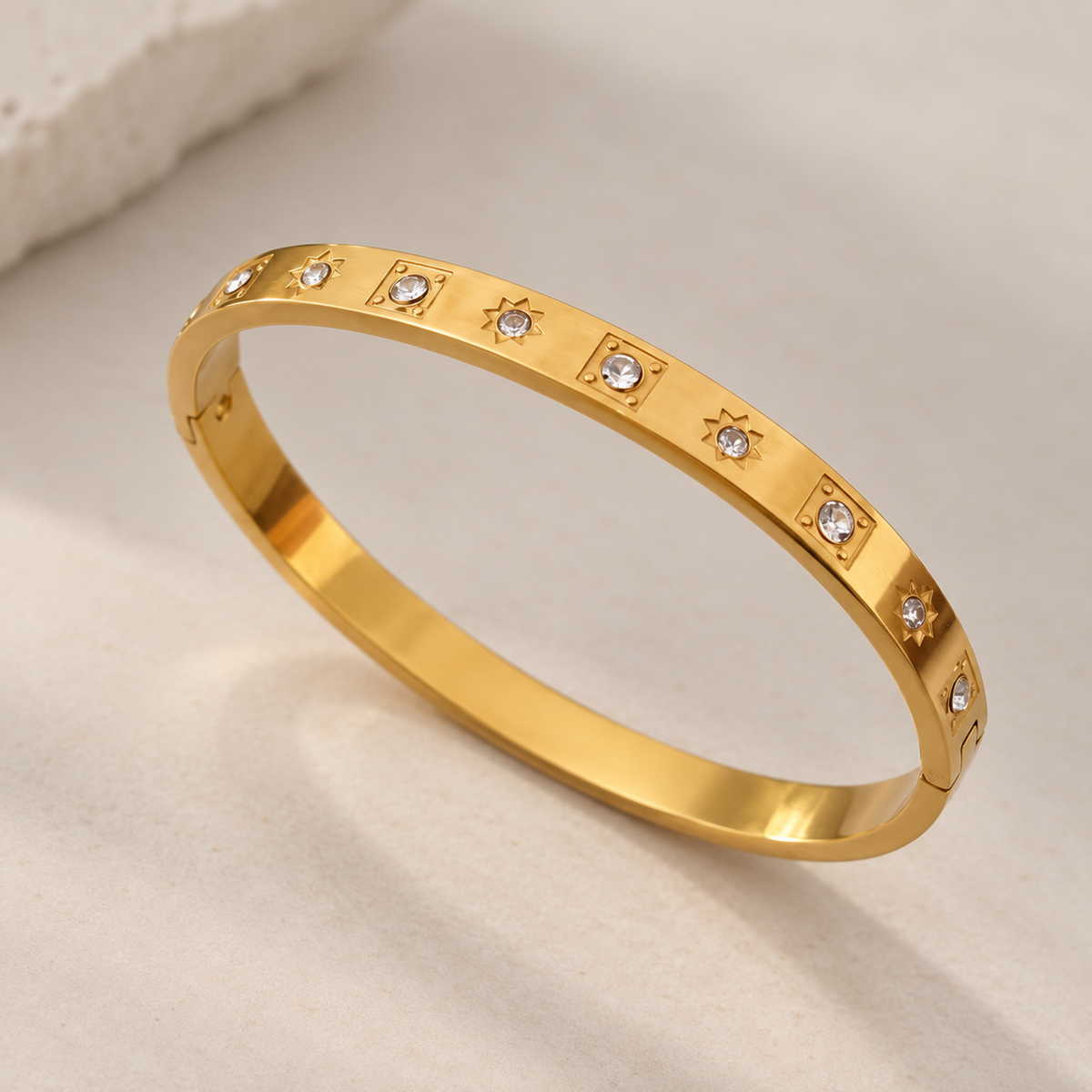 Gold crystal bangle for women with starburst and geometric crystal details and 18kt gold plated finish on a neutral background