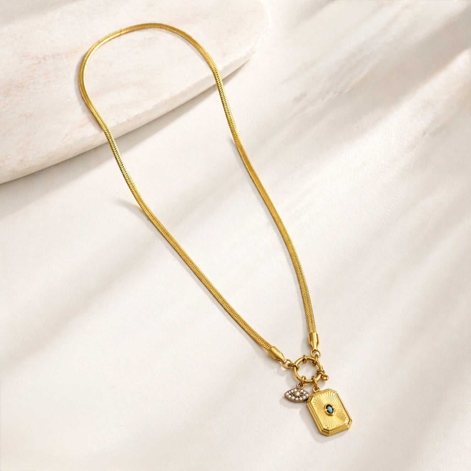 A gold-plated stainless steel chain for women featuring a flat snake chain and two protective charms, including an evil eye medallion