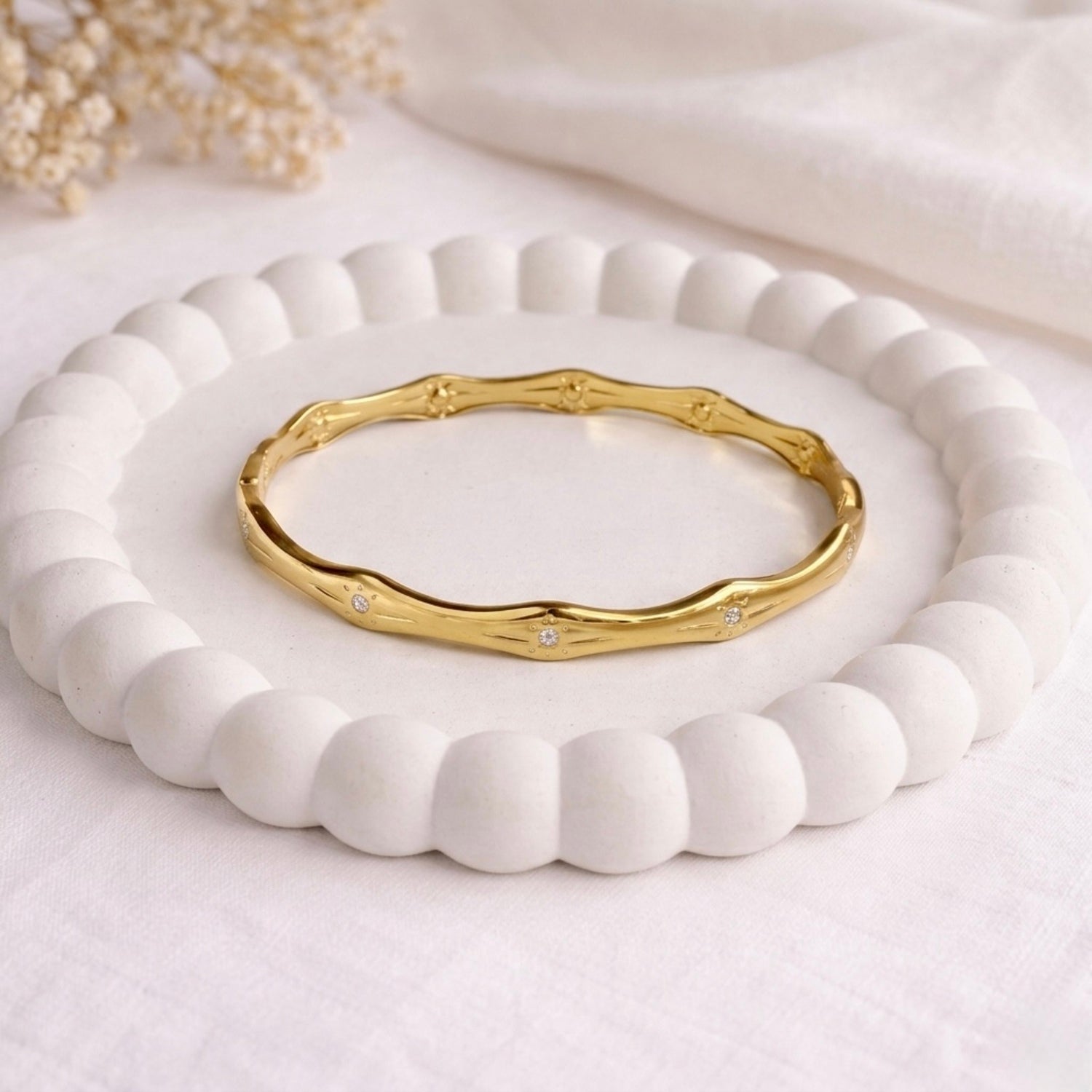 A premium gold-plated bangle for women featuring star-etched engravings and small crystals, displayed on a white ceramic dish.