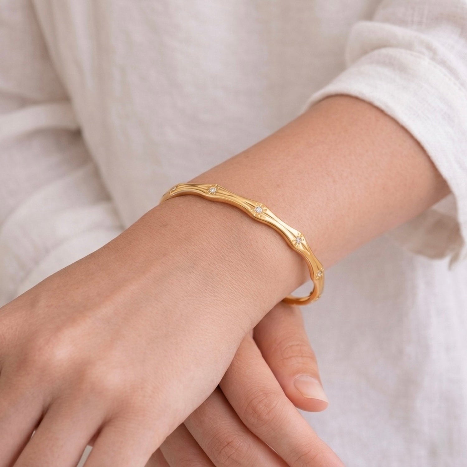A premium gold-plated bangle for women featuring star-etched engravings and small crystals, displayed on a model hand