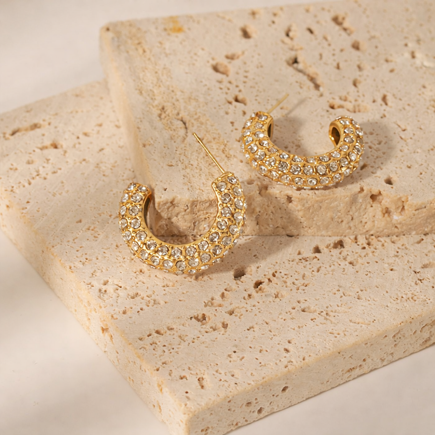 A pair of gold-plated hoop earrings for women featuring a prominent princess-cut clear crystal and smaller round accents on a textured background