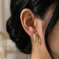 A gold-plated hoop earrings for women featuring a prominent princess-cut clear crystal and smaller round accents, shown on a model