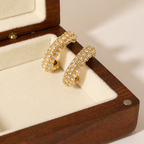 A pair of gold-plated hoop earrings for women featuring a prominent princess-cut clear crystal and smaller round accents on a box