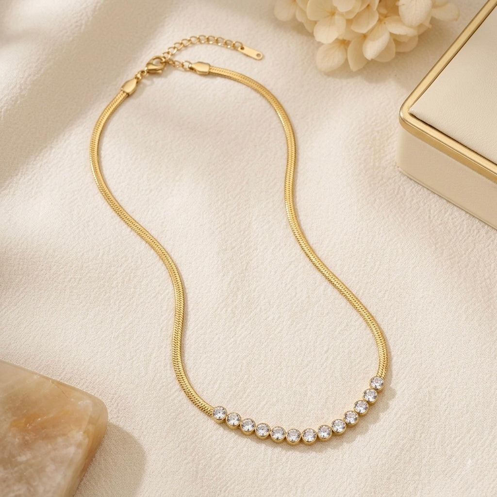 A gold-plated stainless steel snake chain necklace for women featuring a curved row of bezel-set crystals